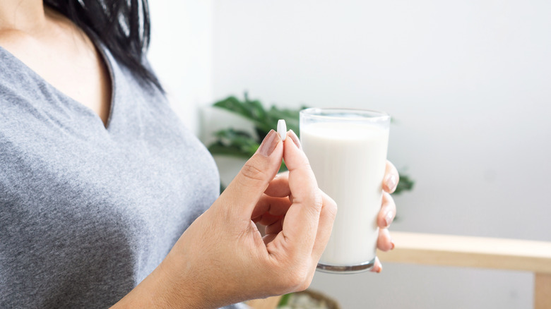 Woman holding pill and glass of milk