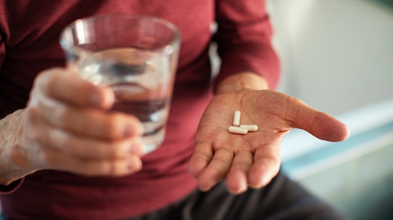 man's hand holding supplements and glass of water