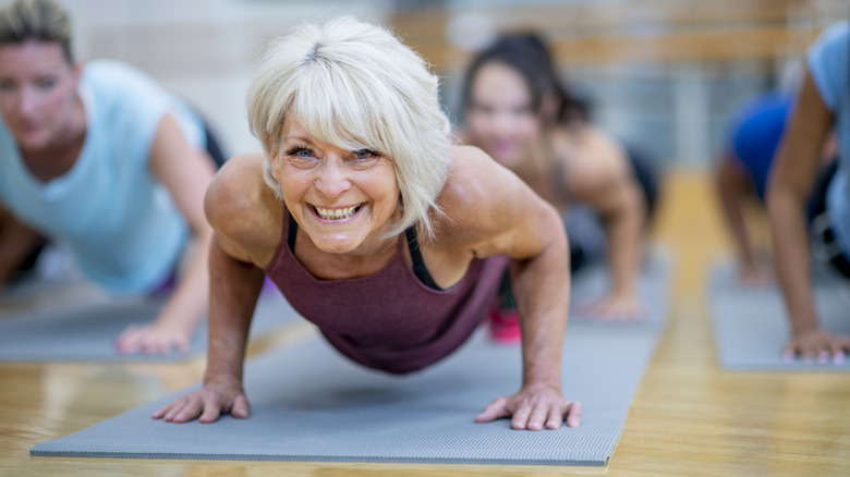 older woman doing yoga pose in a large class