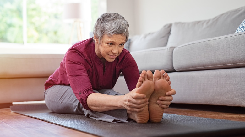 older woman sitting on exercise mat holding toes