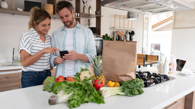 couple looking at phone together in front of vegetables