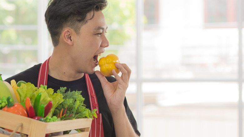 man biting into yellow pepper while holding vegetables