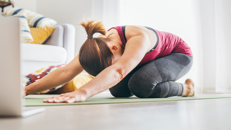 Woman on yoga mat in living room in child's pose