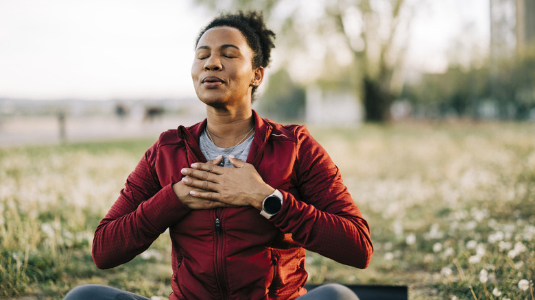 A woman sitting outside with her eyes closed and hands at her heart