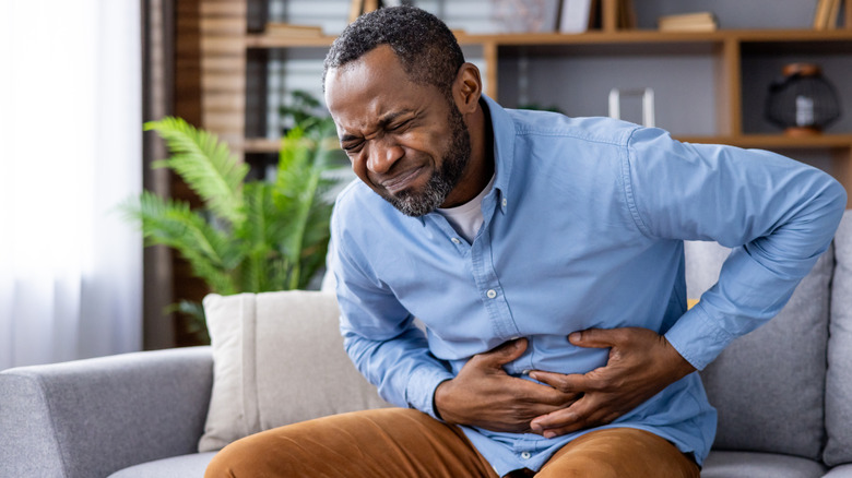 man holding sitting on the couch and holding his stomach in pain