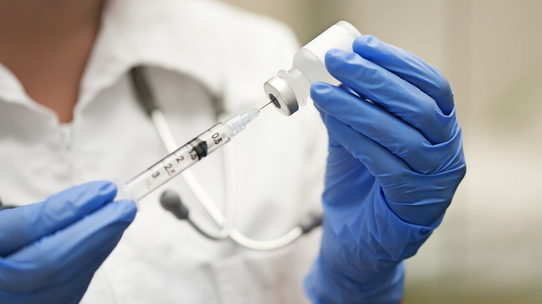 A medical professional withdrawing medicine from a bottle with a syringe