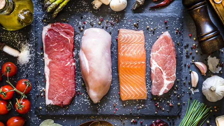 uncooked beef, salmon, chicken, and pork on a cutting board