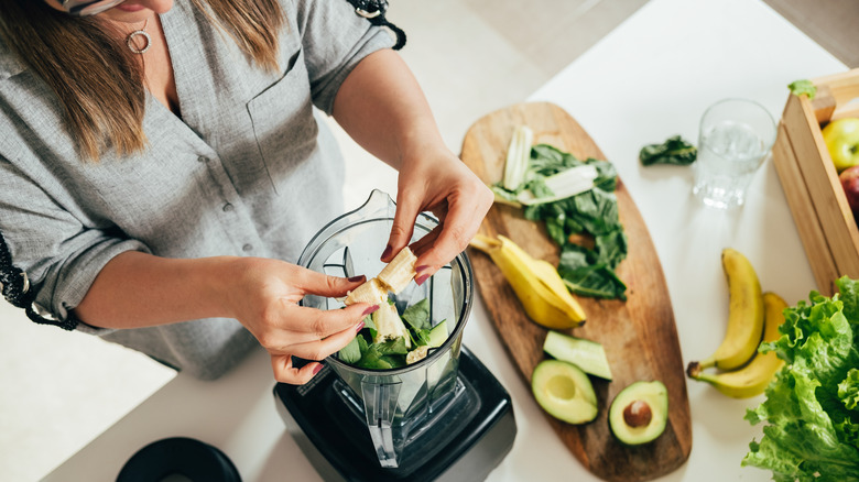 woman preparing a smoothie by adding a banana