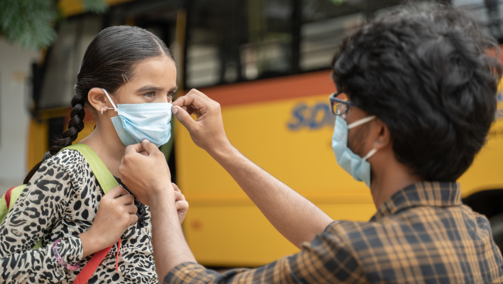 Father helping daughter with mask before getting on the school bus