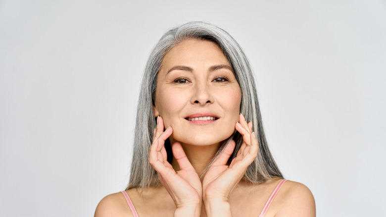 Gray-haired woman smiling and posing with hands near her face