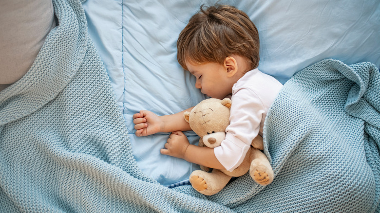 Young boy sleeping in bed with teddy bear.