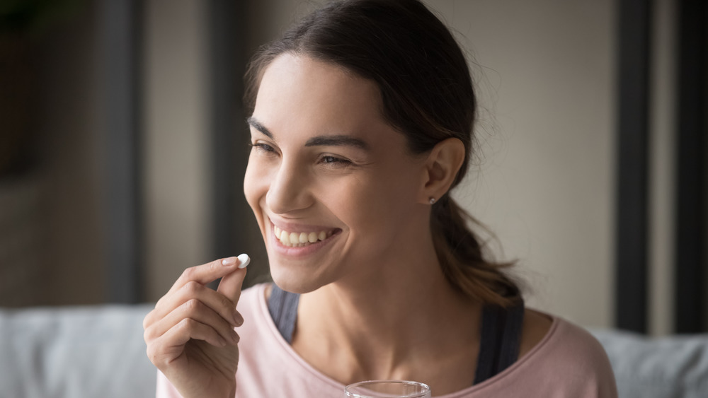 smiling woman taking a supplement with water 