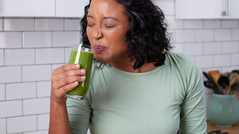 A young woman forcing herself to drink green juice