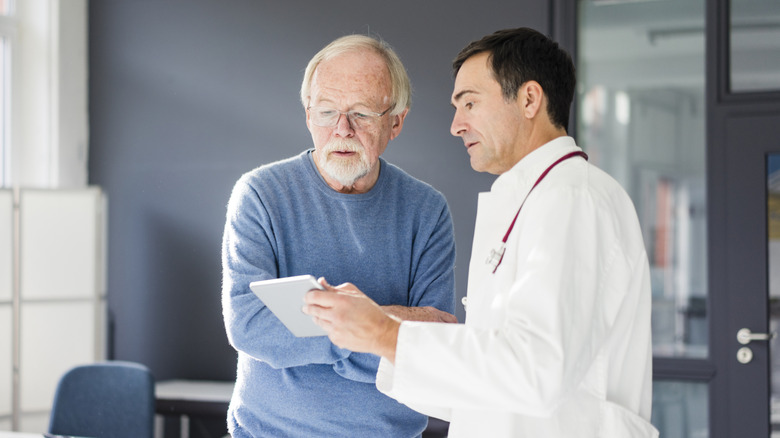 An older man listening to his doctor explain something on the doctor's tablet