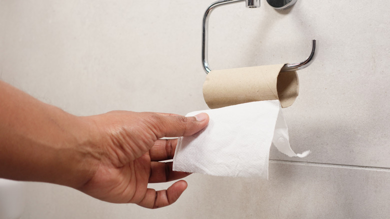 A hand pulling on an empty toilet paper roll