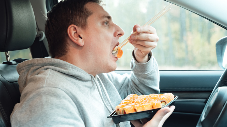 man eating plate of sushi rolls in car