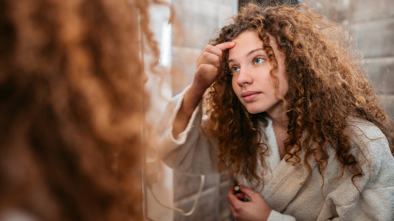 Woman examining forehead in mirror
