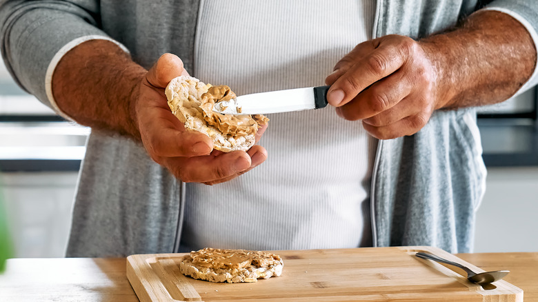 man's hands spreading peanut butter on a rice cake