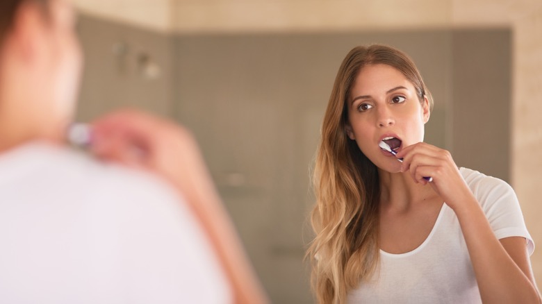 woman brushing teeth in mirror
