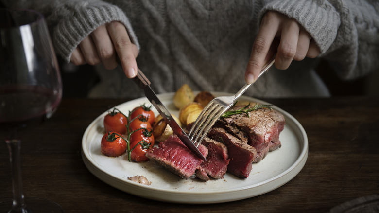 person slicing steak on plate