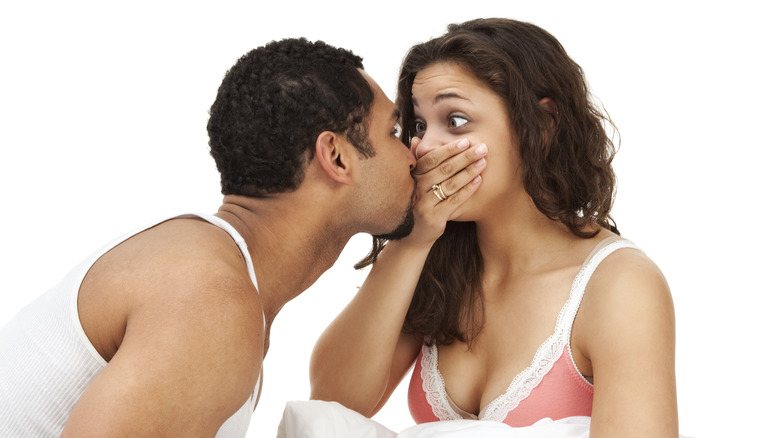 woman holding her hand over her mouth before her boyfriend kisses