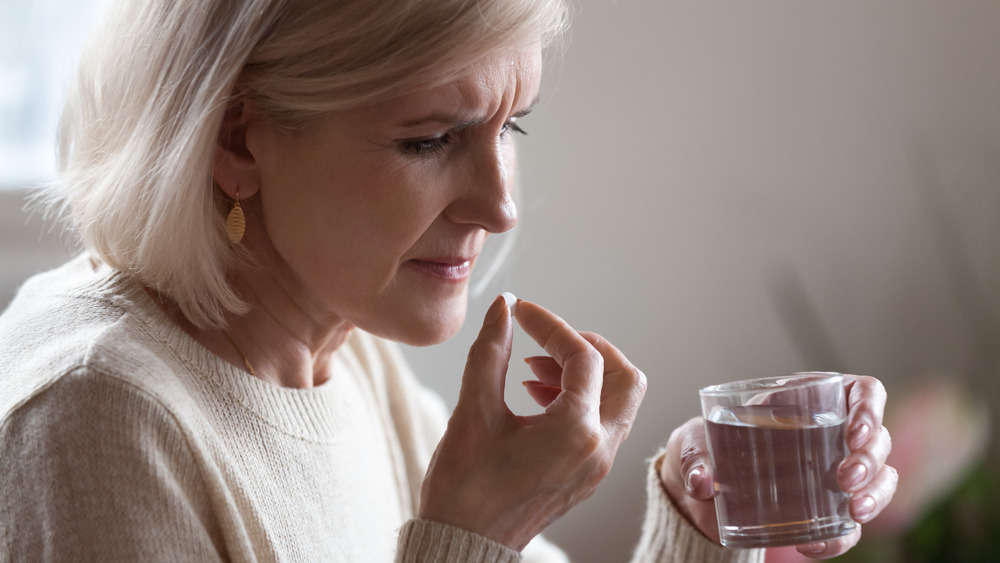 Older woman taking a pill and looking worried