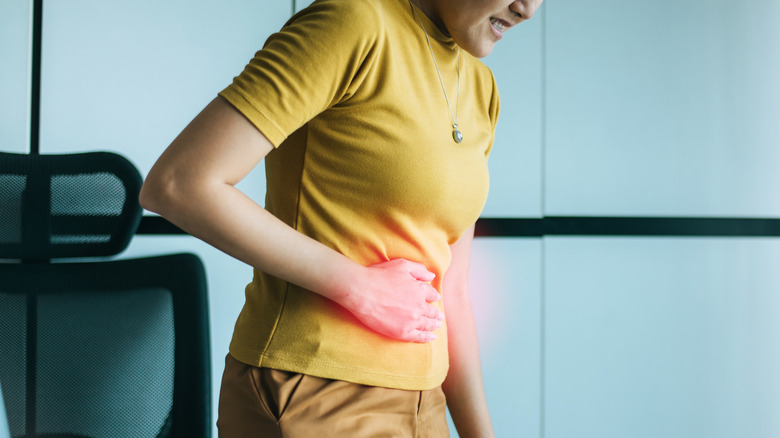 woman standing at desk holding stomach in pain