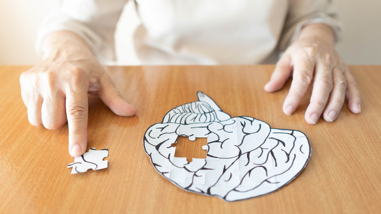 Close up of hands competing a white puzzle shaped like a 2D brain