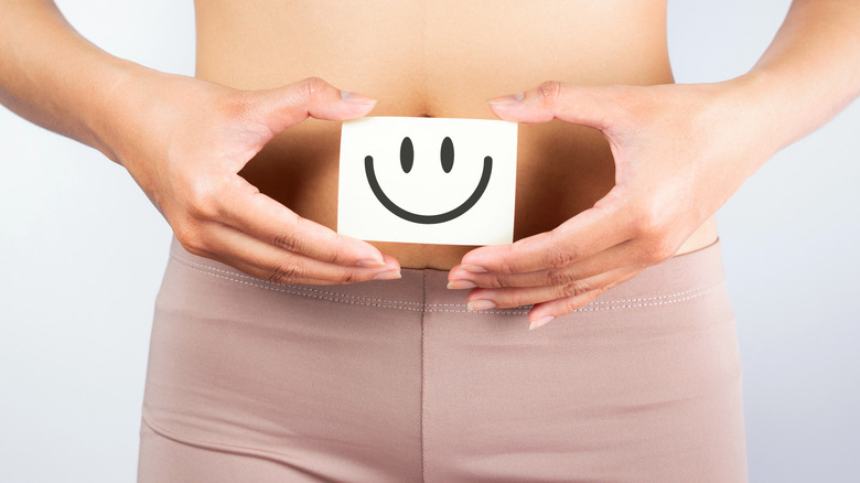 Hands holding a smiley face over their stomach demonstrating a healthy gut