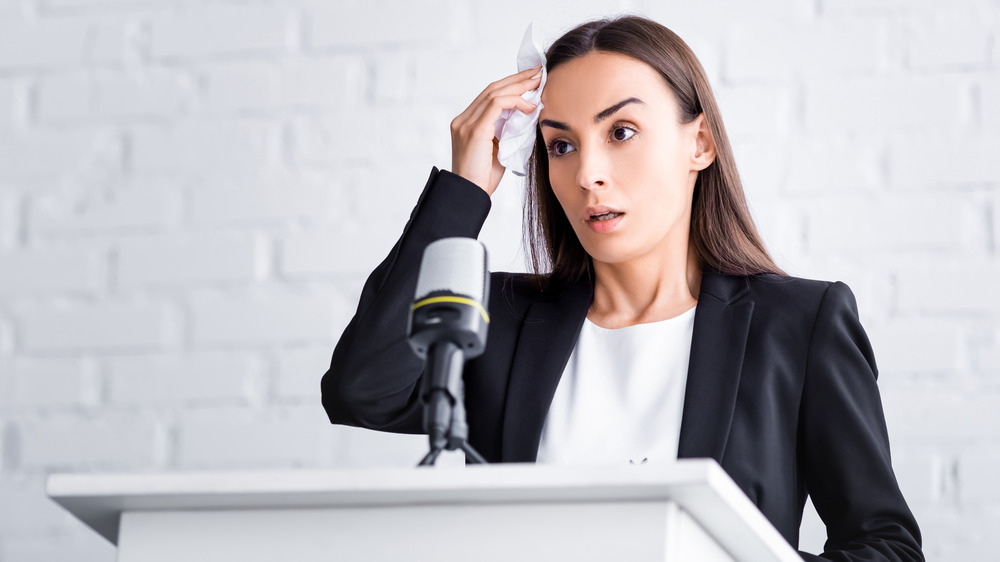 Woman at a podium wiping sweat off forehead