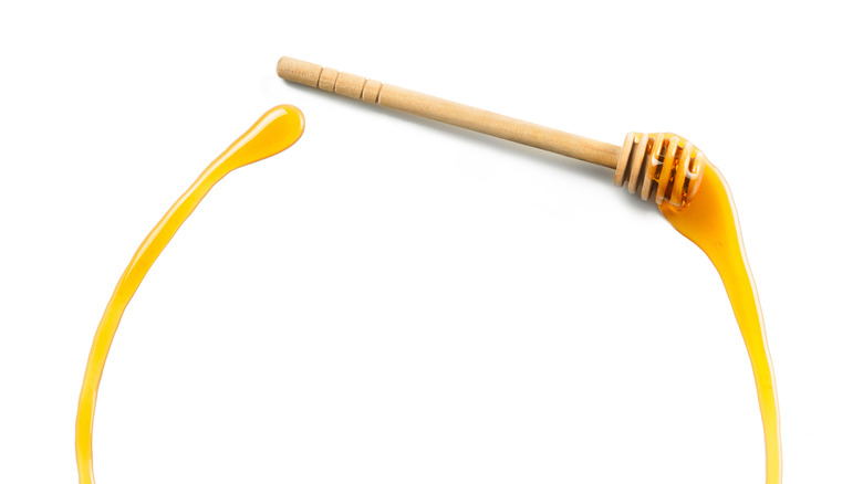 A honey dipper trailing honey on a white surface