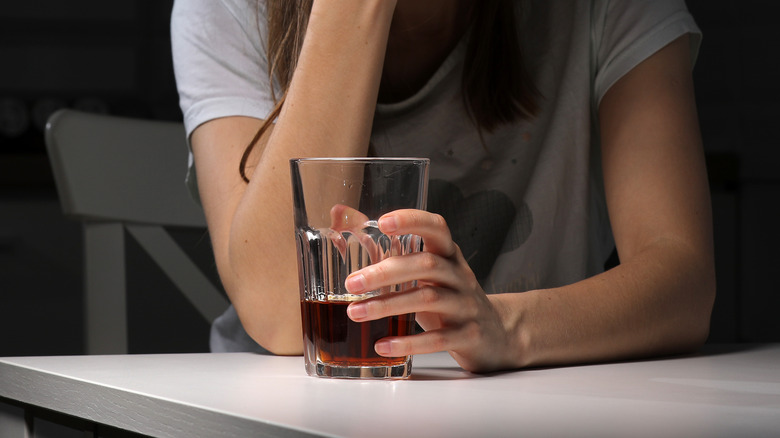 Woman at table holding glass of liquor