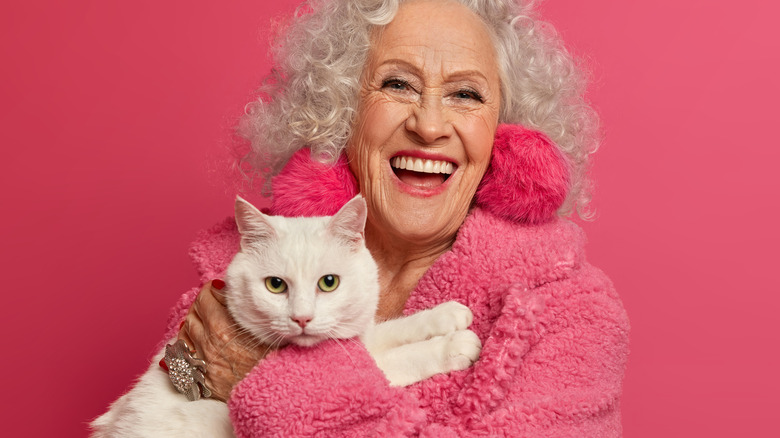 old woman holding cat pink background