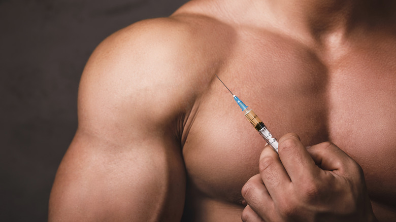 Muscular man holding needle to skin