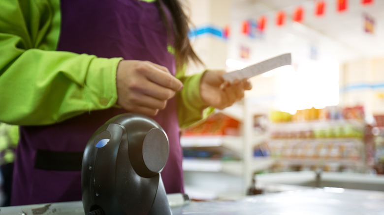 Grocer behind check out counter holding receipt for shopper