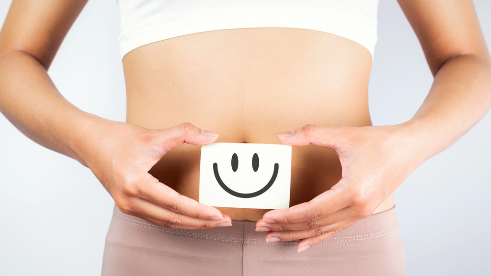 Close up of a woman's belly where she is holding a happy face card