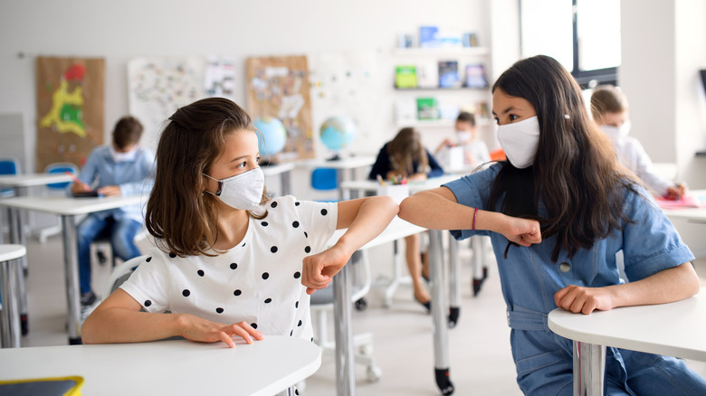 Children wearing face masks touching elbows in a classroom
