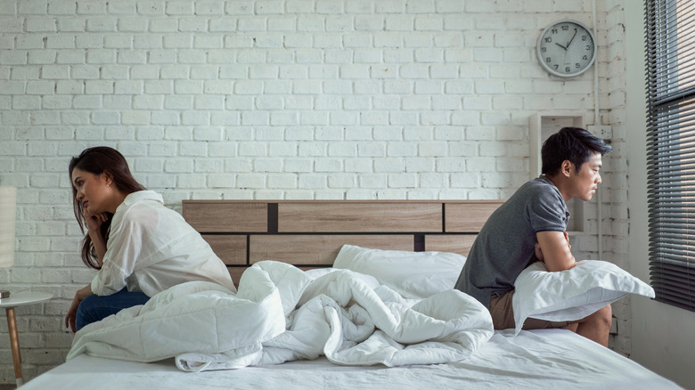 A couple sitting on the far edges of their bed facing away from each other