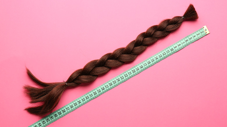 Long brown braid of hair placed next to a measuring tape on pink background