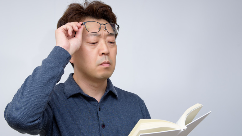 man having trouble reading book