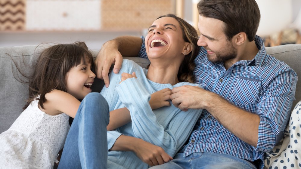 A dad and daughter tickle a mom on the sofa