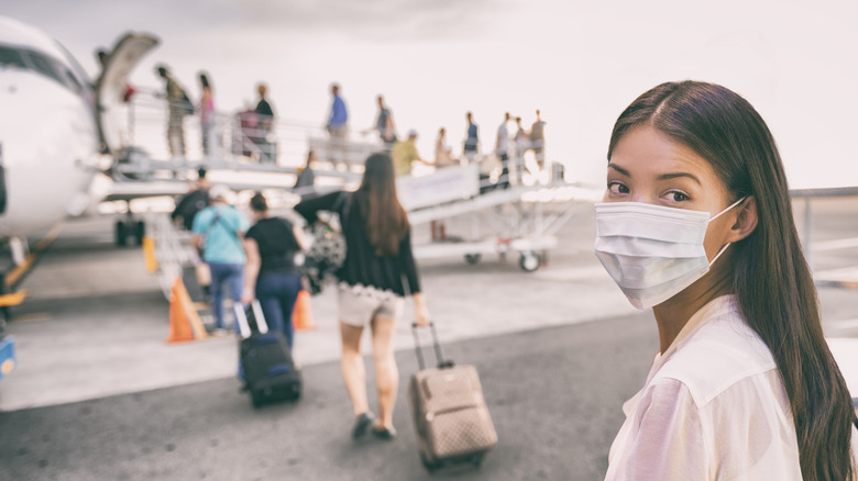 woman tourist boarding plane for holiday wearing face mask