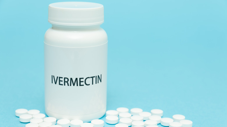 Ivermectin in white bottle packaging with scattered pills on blue background 