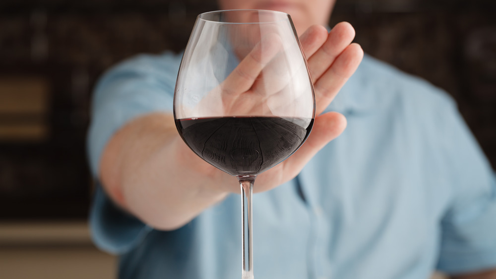 Person refuses glass of wine with hand up