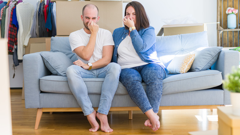 Couple sitting on couch plugging noses with bad smell