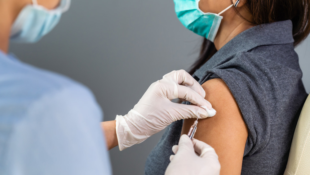 Woman with mask on being vaccinated on arm