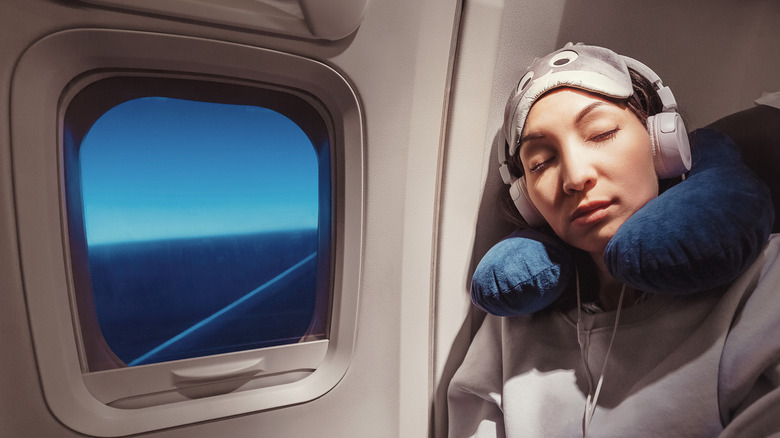 Woman wearing headphones, eye mask, and neck pillow asleep in her seat on a plane