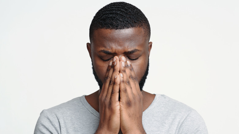 A man with his eyes closed pressing on his nose due to sinus pressure