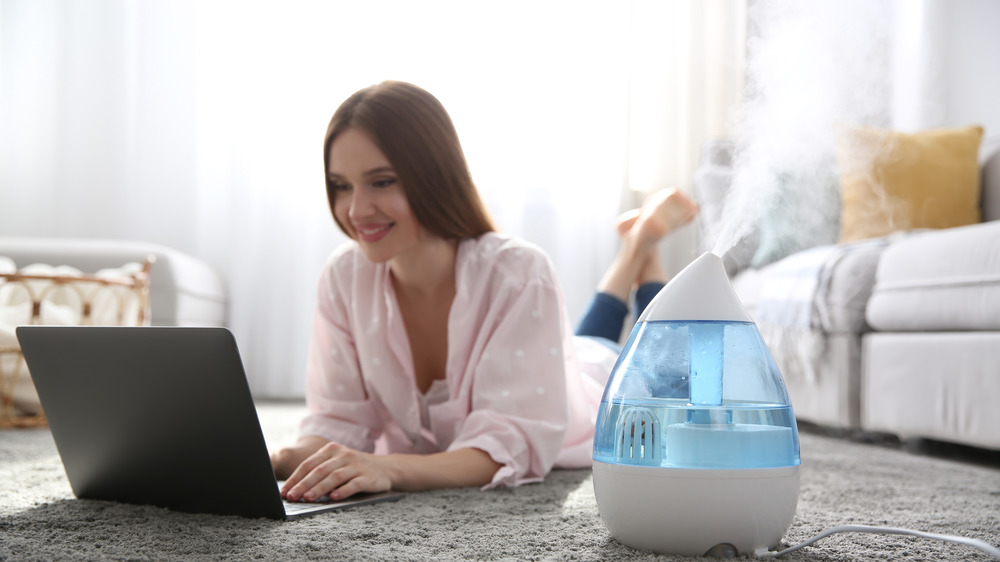 Woman lying on floor typing on laptop next to humidifier