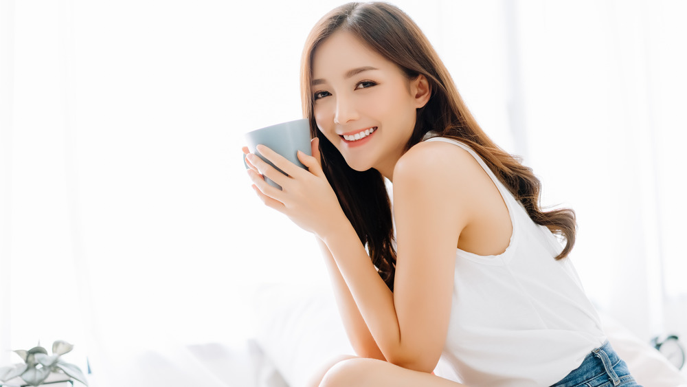 Happy smiling beautiful Asian woman awaking with cup of coffee